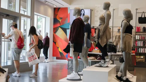 داخل متجر لولوليمون، تظهر دمى عرض ترتدي ملابس رياضية متنوعة، بينما يتسوق زبائن بالقرب من المدخل.