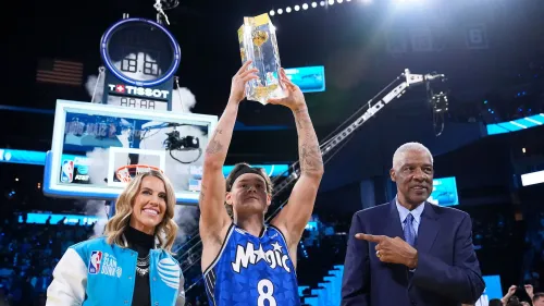 ماك ماكلونج يحمل الكأس بعد فوزه بمسابقة سلام دانك في الدوري الأمريكي للمحترفين، مع الابتسامة واحتفال الحضور في الخلفية.