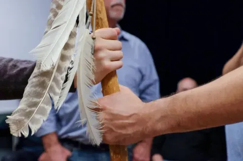 أيدٍ تتبادل عصا تحمل ريشًا، تمثل التواصل والدعم بين الرجال في مجموعة دعم، تعكس أهمية الصداقات العميقة.