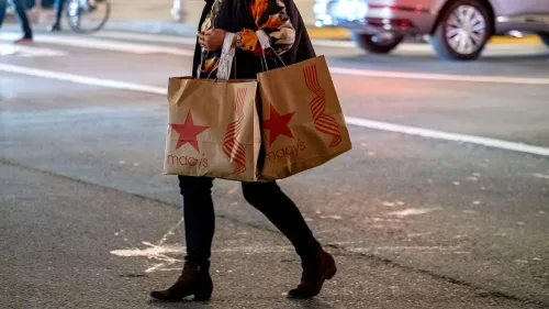 امرأة تحمل أكياس تسوق من متاجر Macy's، تعكس التغييرات في استراتيجية الشركة وسط إغلاقات متاجر جديدة.