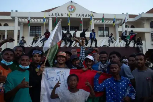 محتجون من جيل مدغشقر يحملون لافتات ويرتدون ملابس سوداء أمام مبنى حكومي، مع تواجد أعلام البلاد في الخلفية.