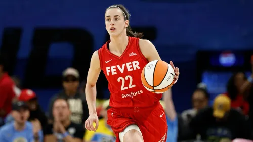 كيتلين كلارك، لاعبة فريق إنديانا فيفر، تحمل كرة سلة أثناء المباراة، مرتدية زي الفريق الأحمر مع الرقم 22، وسط حشد من المشجعين.