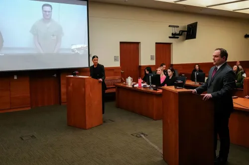 جلسة محكمة تُظهر المتهم مايكل ماكي عبر الفيديو، مع محاميه أمام القاضي، بينما يتواجد آخرون في قاعة المحكمة.