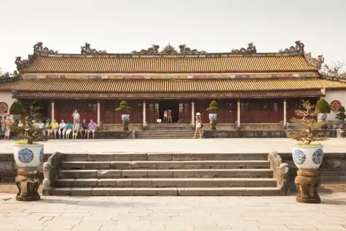 واجهة قصر ثاي هويا في هوي، فيتنام، مع زوار يجلسون على الدرج، يبرز التراث المعماري لأسرة نغوين.