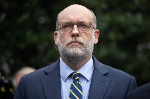 رجل ذو لحية يرتدي بدلة رسمية ونظارات، يظهر بملامح جدية، في خلفية طبيعية، في سياق مرتبط بالتحقيقات الجنائية.