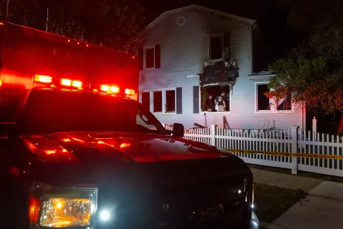 مركبة إطفاء أمام منزل محترق في كوينز، حيث وقع حادث قتل مزدوج لزوجين مسنين، مع وجود رجال الإطفاء في الموقع.