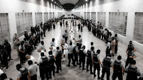 صورة تظهر مجموعة من رجال الشرطة والجنود في سجن، حيث يتجمع المعتقلون في صفوف، مما يعكس الوضع الأمني المشدد في السلفادور.