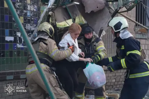 رجال إطفاء يساعدون امرأة على الخروج من مبنى متضرر بعد هجوم بطائرات مسيرة في كييف، مما يعكس آثار الهجمات الروسية على المدنيين.