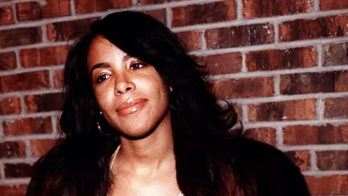 صورة لمغنية الروك آند بي الراحلة آليا، تظهر بابتسامة خفيفة، مع خلفية من الطوب، تعكس إرثها الفني وتأثيرها في الموسيقى.