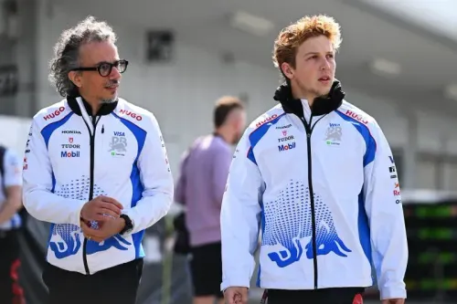 مدير فريق ريد بُل ومساعده يسيران في حلبة سباق، يرتديان ملابس فريق ريد بُل، وسط أجواء سباقات الفورمولا 1.