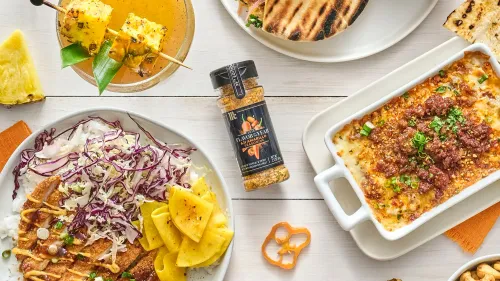 طبق يحتوي على الأرز مع شرائح من اللحم والخضار والفواكه، وزجاجة توابل آجي أماريلو بجانب الأطباق، يعكس التنوع في المأكولات العالمية.