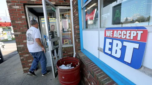 لافتة على واجهة متجر تشير إلى قبول بطاقات EBT، بينما يدخل رجل إلى المتجر. تعكس الصورة القضايا المتعلقة ببرامج الدعم الاجتماعي.
