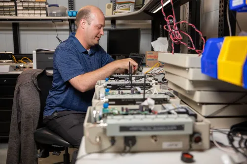 رجل يعمل على تجهيز أجهزة قياس البرق في مختبر، مع وجود معدات إلكترونية مرتبة على الطاولة، مما يعكس جهود البحث في ظاهرة البرق الضخم.