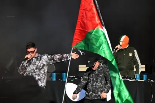 يظهر في الصورة أعضاء فرقة "كنيكاب" يؤدون عرضًا موسيقيًا، بينما يرفع أحدهم علم فلسطين. تعكس الصورة دعمهم للقضية الفلسطينية وسط جدل حول التهم الموجهة لأحدهم.