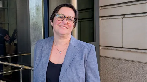 كاثي هاريس، رئيسة مجلس حماية أنظمة الاستحقاق، تقف مبتسمة أمام مدخل المكتب بعد قرار قضائي يسمح لها بالبقاء في منصبها.