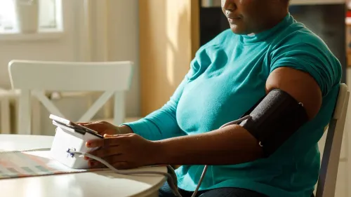 امرأة ترتدي قميصًا أزرق وتستخدم جهاز قياس ضغط الدم في منزلها، مما يعكس أهمية متابعة الصحة لاستباق مشاكل متلازمة الأيض.