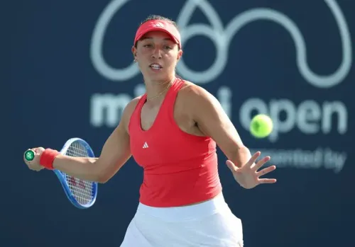 لاعبة تنس ترتدي زيًا أحمر، تستعد لضرب كرة التنس خلال بطولة ميامي المفتوحة. تعكس الصورة التوتر والتركيز في المباراة.