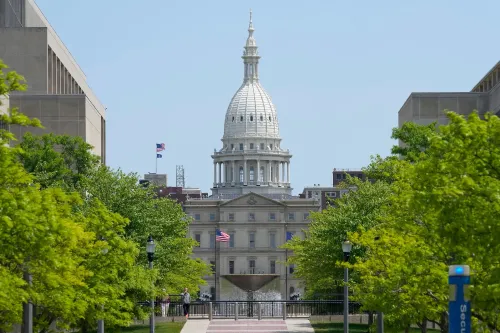 مبنى الكابيتول في ولاية ميشيغان يظهر وسط الأشجار الخضراء، يرمز إلى الأحداث القانونية المتعلقة بانتخابات 2020.