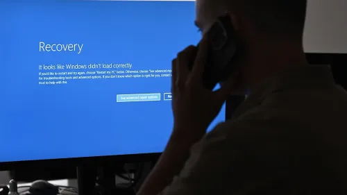 شاشة زرقاء تعرض رسالة "استعادة" تفيد بأن نظام ويندوز لم يتم تحميله بشكل صحيح، مع شخص يتحدث في الهاتف.