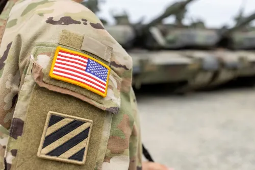 شعار عسكري أمريكي على زي جندي، مع خلفية تضم دبابات عسكرية، يعكس تأثير الإغلاق الحكومي على العائلات العسكرية.