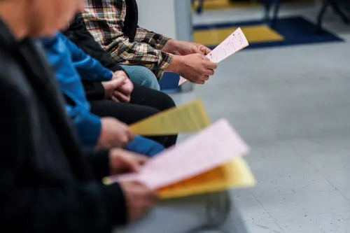 أشخاص يجلسون في قاعة انتظار، يحملون أوراقًا ملونة تتعلق بتغطية الرعاية الصحية، تعبيرًا عن قلقهم بشأن الإعانات المعززة.