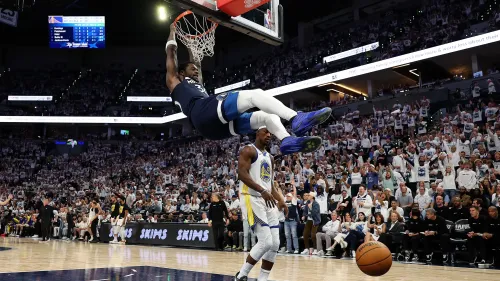 لاعب من فريق مينيسوتا تيمبروولفز يقوم بسلة مذهلة أثناء مباراة ضد جولدن ستيت ووريورز، مع جمهور متحمس في الخلفية.