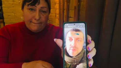 امرأة تحمل هاتفًا ذكيًا يعرض صورة لرجل، في سياق البحث عن مفقودين في الحرب الأوكرانية، تعبيرها يعكس القلق والأمل.