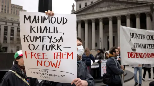 لافتة في احتجاج تطالب بالإفراج عن محمود خليل وروميسا أوزتورك، مع وجود متظاهرين خلفها في ساحة عامة.