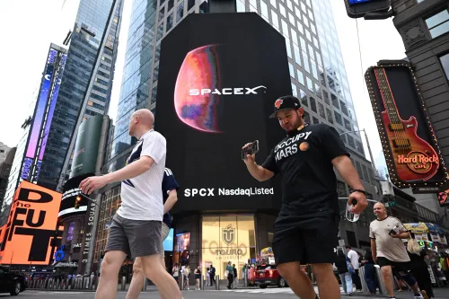 شاشة ضخمة تعرض شعار SpaceX وسط مبانٍ في تايمز سكوير مع مشاة يمرون، تعكس تداول أسهم SpaceX وتأثيرها في السوق.
