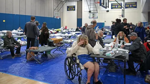 أشخاص في مأوى للاجئين يجتمعون حول طاولات، مع أسرة مؤقتة مرتبة في الخلفية، وسط أجواء من التوتر بسبب حرائق الغابات في لوس أنجلوس.