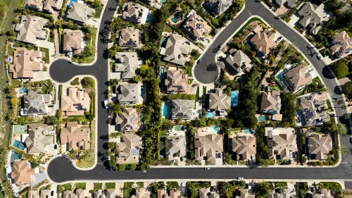 مشهد جوي لحي سكني يتضمن منازل متعددة مع مسارات طرق متعرجة، يعكس تأثير معدلات الرهن العقاري المرتفعة على سوق الإسكان.