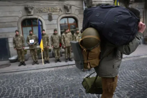 جندي أوكراني يحمل حقيبة كبيرة ويرتدي خوذة، بينما يقف جنود آخرون في صف خلفه، في مشهد يعكس الوضع العسكري في أوكرانيا.