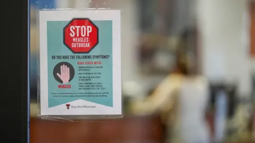 ملصق يحذر من تفشي الحصبة، يوضح الأعراض ويحث على الاتصال بالعيادة في حال ظهورها، مع خلفية غير واضحة لشخص في مكتب.