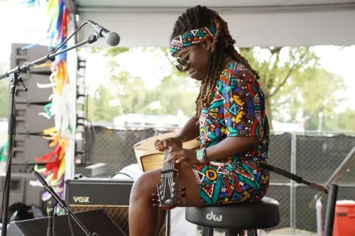 موسيقية ترتدي ملابس ملونة وتجلس على الكرسي أثناء العزف على آلة موسيقية، محاطة بأجواء حيوية في حدث موسيقي.