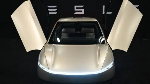 سيارة تسلا الكهربائية مع أبواب تفتح لأعلى، تعرض تصميمها العصري في حدث ترويجي، مع خلفية تحمل شعار تسلا.