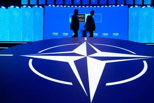 شعار حلف الناتو مضاء بالأزرق مع ظلّ شخصين في مؤتمر يعكس تحذيرات الحلف من تهديدات إيرانية متزايدة في أوروبا.
