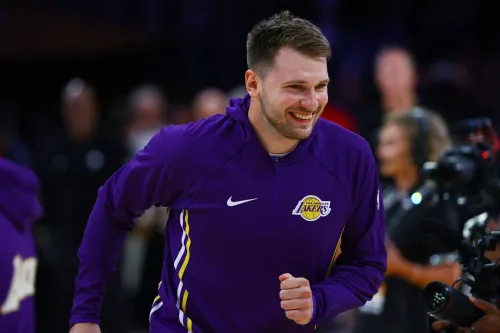 لاعب كرة سلة مبتسم يرتدي زي فريق لوس أنجلوس ليكرز، يستعد للمباراة مع خلفية من الجماهير في الملعب.