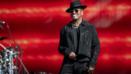 ني-يو يبتسم ويرتدي ملابس أنيقة خلال أدائه، مع خلفية حمراء لامعة، معبرًا عن ثقته في حياته العاطفية غير التقليدية.