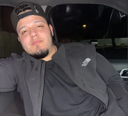 صورة لرجل يجلس في سيارة، يرتدي سترة سوداء وقبعة، مع تعبير جاد على وجهه، تعكس موضوع الترحيل والمهاجرين.