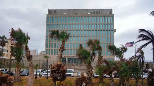 مبنى سفارة الولايات المتحدة في هافانا، محاط بأشجار النخيل، مع أعلام أمريكية ترفرف في الخلفية، في سياق التحقيقات حول متلازمة هافانا.