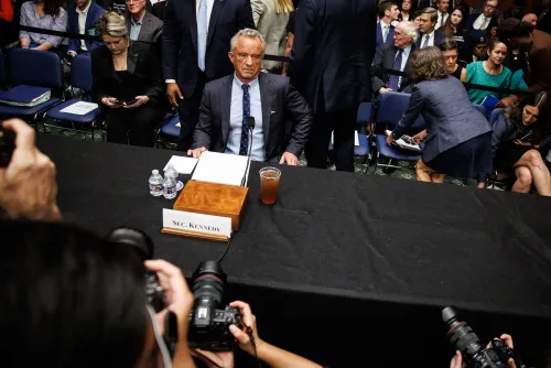 روبرت كينيدي جونيور جالس أمام طاولة خلال جلسة استماع، محاطًا بالحضور والمصورين، في سياق مناقشات حول الصحة العامة.