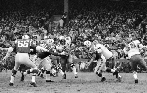 لقطة تاريخية لمباراة كرة قدم أمريكية، حيث يتنافس فريق نيو أورليانز ساينتس ضد فريق آخر، مع وجود مشجعين في المدرجات.