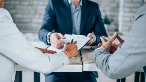 اجتماع لمناقشة تفاصيل ضريبة التركات، حيث يظهر شخصان يتبادلان الوثائق مع مستشار قانوني، مع التركيز على أهمية الإعفاءات الضريبية.