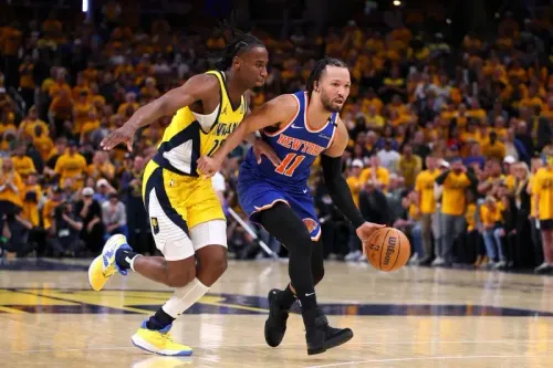 لاعب نيويورك نيكس يحمل الكرة بينما يطارده لاعب إنديانا بيسرز، مع جمهور متحمس في الخلفية خلال مباراة حماسية في التصفيات.