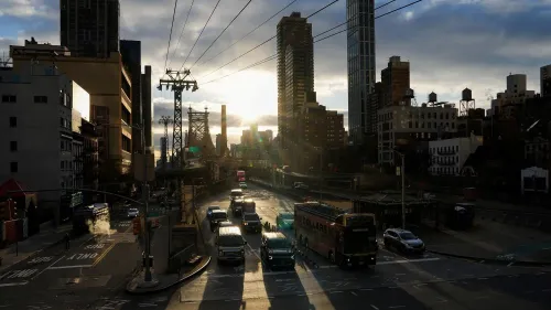 مشهد لشارع مزدحم في مدينة نيويورك عند غروب الشمس، مع سيارات وشاحنات تمر بجوار المباني الشاهقة، مما يعكس تحديات تسعير الازدحام المروري.