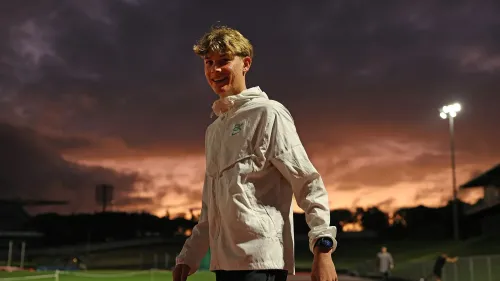 سام روثي، الرياضي النيوزيلندي، مبتسم بعد تحقيقه إنجاز الركض لمسافة ميل في أقل من أربع دقائق، وسط أجواء غائمة في الملعب.