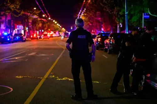 شرطي من شرطة فانكوفر يقف في موقع حادث مأساوي بعد اصطدام سيارة بحشد في مهرجان، مع وجود سيارات إسعاف وأضواء الطوارئ في الخلفية.