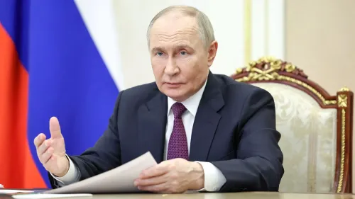 فلاديمير بوتين يجلس خلف مكتب، معبرًا عن موقفه خلال اجتماع، بينما تبرز الأعلام الروسية خلفه، مما يعكس سياسته في الحرب على أوكرانيا.