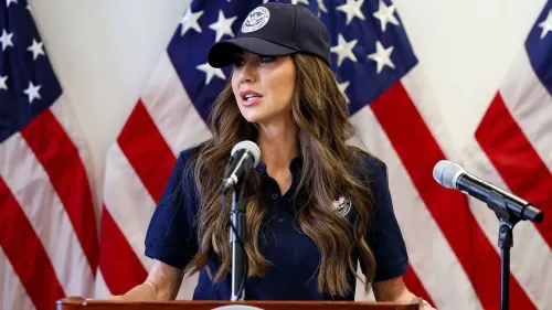 وزيرة الأمن الداخلي كريستي نويم تتحدث أمام الميكروفون، مع العلم الأمريكي خلفها، أثناء إعلان عن تغييرات في سياسة التمويل.