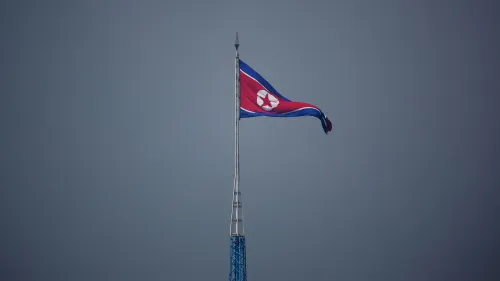 علم كوريا الشمالية يرفرف فوق عمود في سماء رمادية، يمثل رمزاً للسيادة الوطنية، بالتزامن مع استعدادات الماراثون الدولي في بيونغ يانغ.